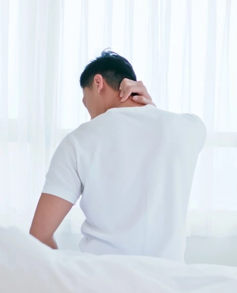아침에 침대에서 일어나 목 결림을 느끼는 남성 이미지 – 코골이 수면 질 저하