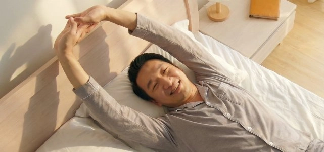 유프니아 사용 후 개운하게 아침에 기지개를 켜며 일어나는 남성 이미지